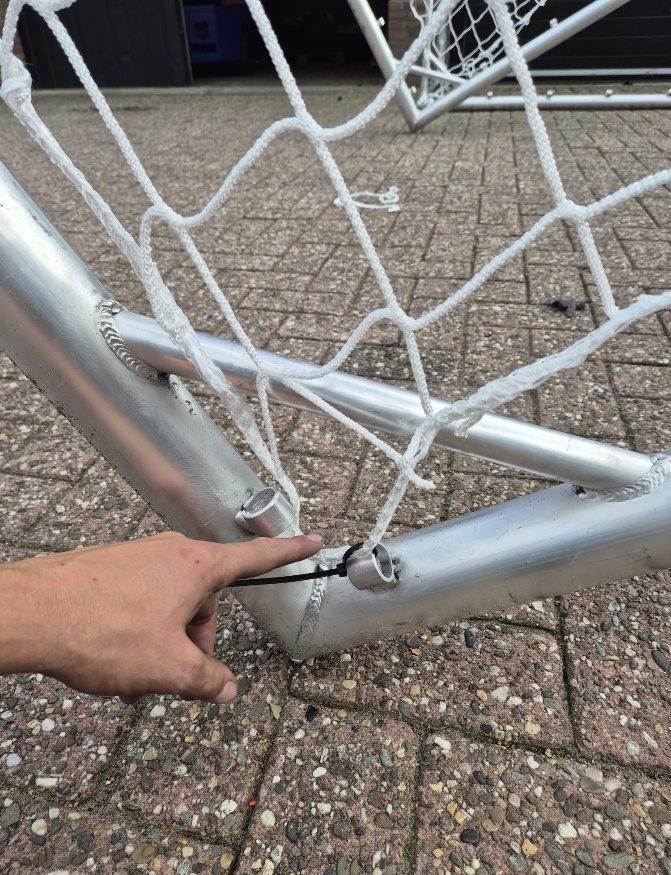 Hand zet het net met een tiewrap vast in de hoek van het doel